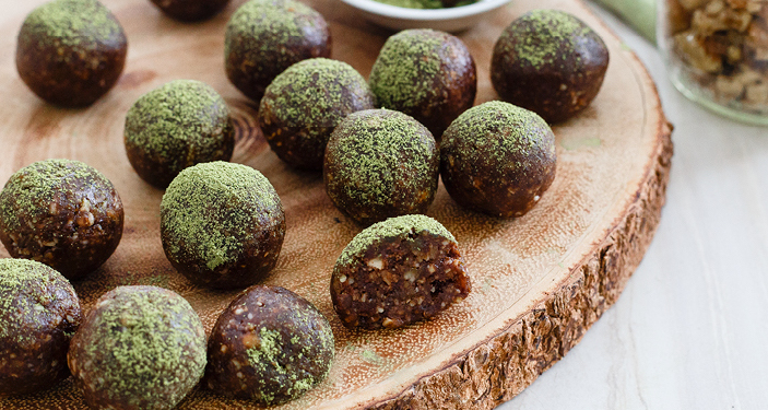 Chocolate energy balls, dusted with matcha powder on a board.