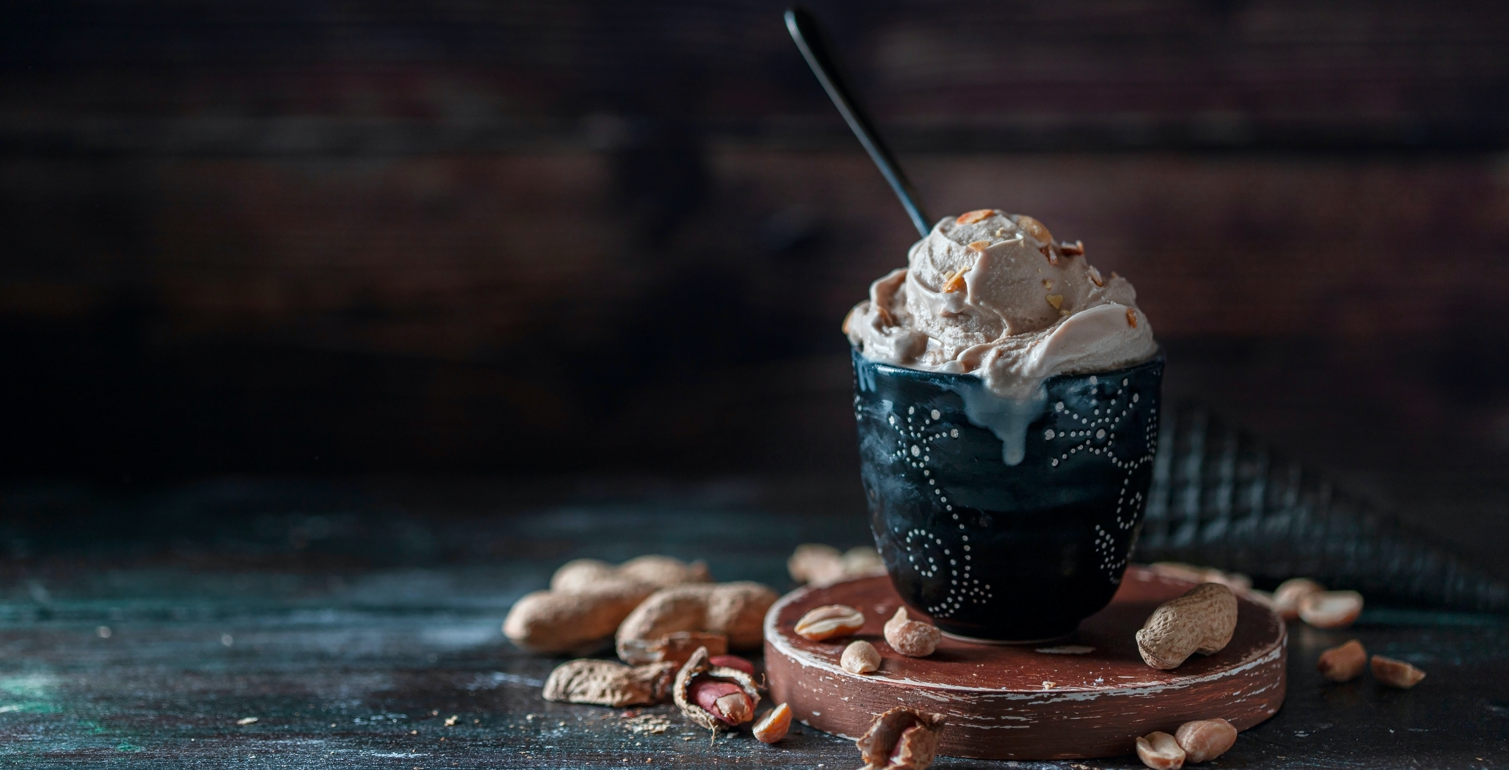 picture of peanut butter ice cream in a pot, on a wooden board, with a spoon.